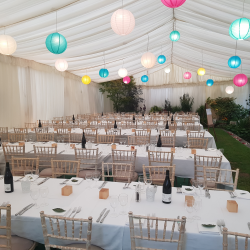 Chiavari chairs with trestle tables in a clearspan marquee decorated with lining and lanterns, for a wedding in Bath