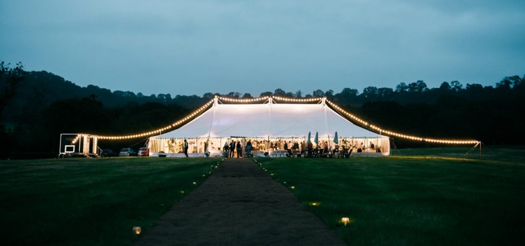 Festoon lighting over the top of a traditional marquee, with a coconut matting pathway provided by Archers Marquees in Somerset