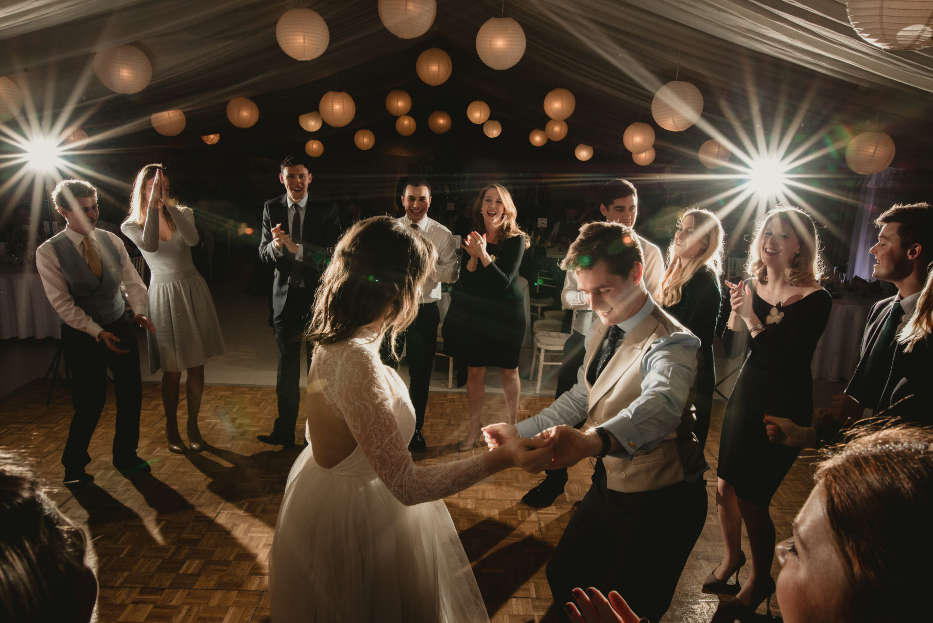 White paper lanterns at night, above a wooden parquet dancefloor in a lined sports hall. Installed by Archers Marquees at Prior Park College